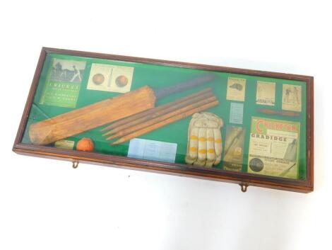 A cricketing montage, glazed and cased for wall mounting, including a cricket bat and stumps, glove and ball, and printed ephemera, 43cm H, 106cm W.