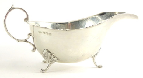 A George V silver sauce boat, with a shaped edge, scroll handle and shaped legs, headed by leaf casting, Birmingham 1920, 4½ oz.