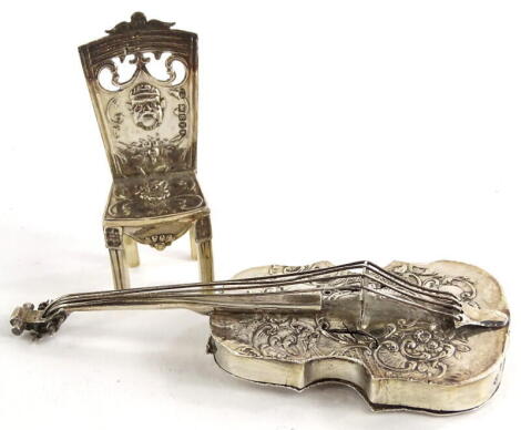 A continental white metal pill box, modelled in the form of a violin or cello, with embossed and cast decoration of scrolls, flowers, etc., possibly Dutch, London import marks, and a similar miniature chair, stamped to the reverse Granada 1908, 2oz, (2).