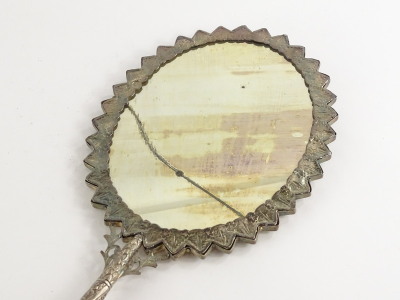 An eastern silver coloured metal hand mirror, embossed with flowers, leaves, etc., and with a jagged edge to the oval frame, mirror plate cracked, (AF). - 2