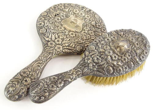 An Edwardian silver hand brush, embossed with flowers, scrolls and leaves, surrounding a vacant cartouche and a matching hand brush, Chester 1905, (2).