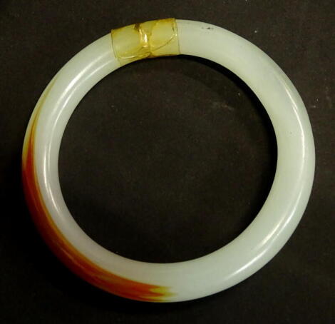 A modern jade bangle, of pale green and orange colour, (AF), 47.2g all in.