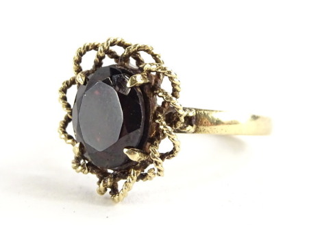 A 9ct gold garnet dress ring, with central oval garnet in four flaw setting, with twist design floral border, ring size N, 3.6g all in.