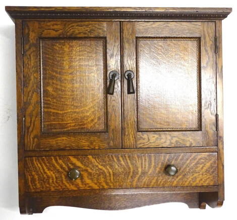 A 1920s/1930s oak wall cabinet, with two panelled doors, each with green Bakelite handles enclosing a fitted interior above a drawer with similar square section handles, 46cm high, 43cm wide.