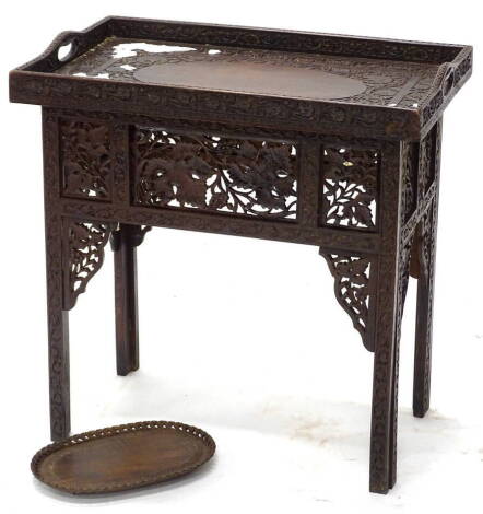 An Indian hardwood tray table, profusely carved with flowers, leaves, etc., around a vacant oval central section, the stand decorated with grapes and vines, 61cm high, 61cm wide, and a similar small tray (2).