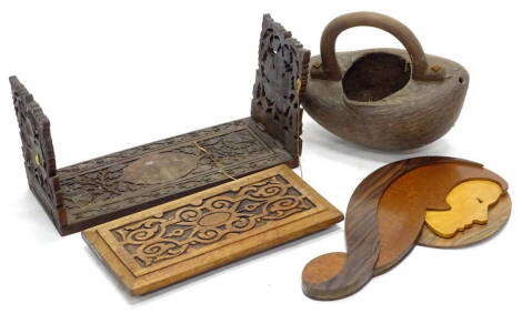 An eastern bag or trug, formed from a nut, with loop handle, an Art Deco coromandel and specimen timber inlaid masked wall plaque, a carved kettle stand, and an Indian adjustable book rack, carved with grapes and vines, (4).