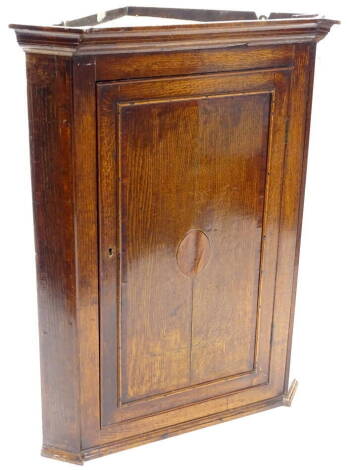 An early 19thC oak and mahogany cross banded corner cabinet, with a moulded inverted breakfront cornice above a single panelled door, inlaid with an oval, enclosing a fitted interior, 108cm high, 86cm wide.