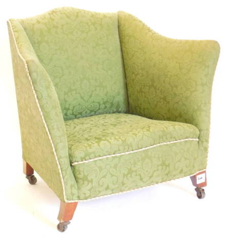 An early 20thC mahogany tub shaped arm chair, upholstered in green patterned damask, with multicoloured piping, with splayed legs and metal castors.