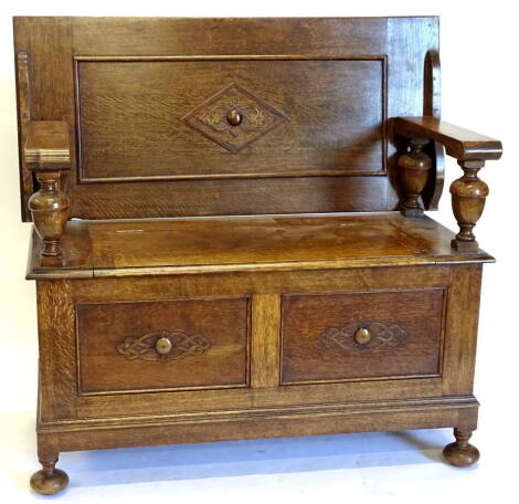 A 1920's oak monks bench, the rectangular top with a moulded edge, on cup and cover turned supports, with hinged seat and bun feet, 106cm wide.