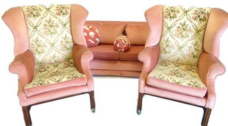 A pair of mahogany wing back chairs, each upholstered in pink and gold floral pattern fabric, on channelled legs with castors and a pink sofa (3). The upholstery in this lot does not comply with the 1988 (Fire & Fire Furnishing) Regulations, unless sold t