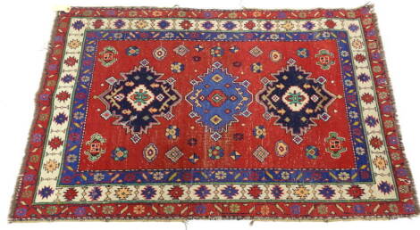 A Kazak type rug, with three brightly coloured medallions, on a red ground, embellished with geometric devices, three borders, 147cm x 101cm.