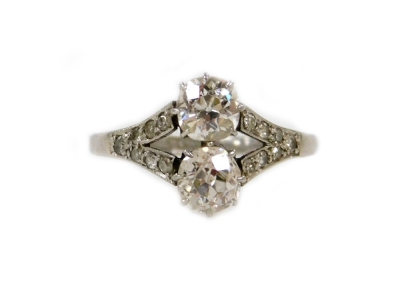 An Art Deco diamond ring, set with two old round cut stones of 8.5mm diameter each, split shoulders set with seven tiny stones of 1mm, shank stamped PLAT., size N-O, in a Garrard & Co articulated box.