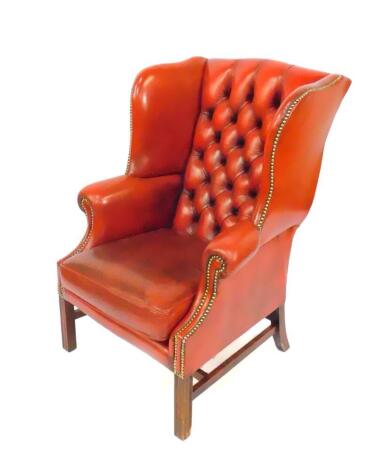 An oak framed red leather button back wing armchair, with loose cushion seat, and brass stud work, raised on fluted square legs, united by an H frame stretcher.