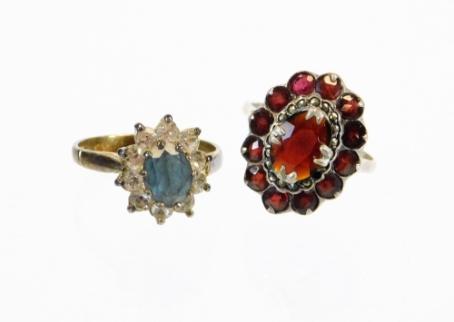 Two dress rings, to include a silver and red stone floral cluster ring, and a blue and white stone cluster ring, on white metal, unmarked.