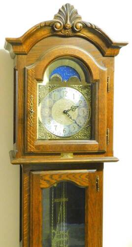 An oak finish longcase clock, with scroll and shell hood, arched glass door and panel base, 22cm arched dial and moon rolling action, with three weights and pendulum, 193cm high.