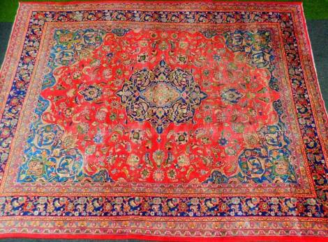 A 20thC Iranian carpet, of rectangular form with outer floral field predominantly in red, blue and green, with a floral centre, 380cm x 290cm.