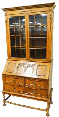 A 20thC oak bureau bookcase, the upper section with fixed cornice, raised above two glazed doors, the subsection with a carved fall, raised above four drawers, on barley twist legs and compressed bun feet joined by barley twist stretchers, 221cm high, 111