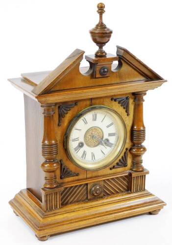 An Edwardian oak cased mantel clock, in an architectural case with broken pediment, surmounted by an urn finial, raised above an 11cm diameter Roman numeric dial with raised spandrels, the stepped based terminating in compressed bun feet with an eight day