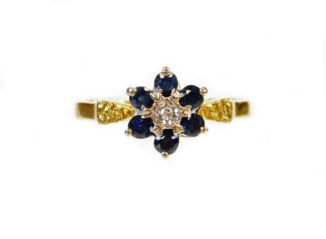 An 18ct gold dress ring, florally claw set with white and blue stones with textured shoulders on a plain shank, size L-M, 3g all in.