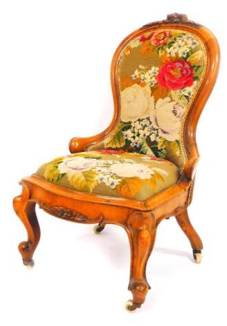 A Victorian walnut nursing chair, the heavily carved spoon back and seat in petit point floral pattern, on squat cabriole front legs, terminating in castors with a central carved section, 88cm high.