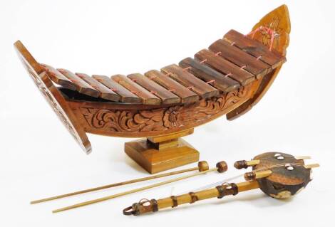 A 20thC Cambodian xylophone, in the form of a boat, with heavily carved body on plain square base, 32cm high.