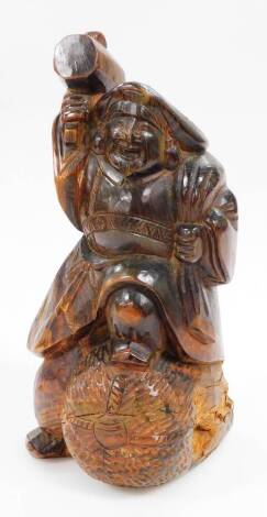 A Japanese wood carving of a Daikoku in flowing robes, holding his mallet, with his foot on a bale of rice, 26cm high.