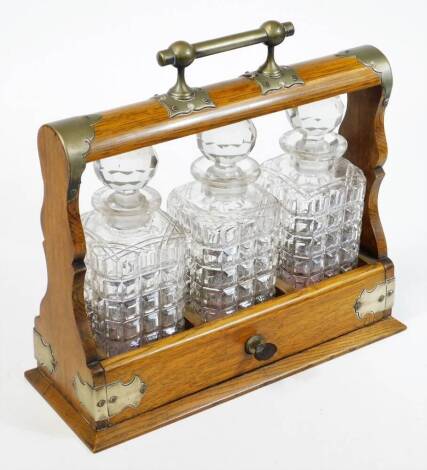 An Edwardian oak framed tantalus, with plated mounts, three moulded and cut finish glass decanters having facet cut stoppers, replacement key, 34cm high, 36cm wide.