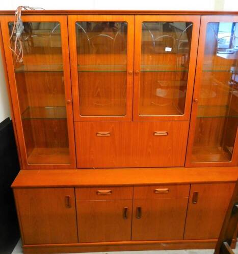 A retro teak room unit, centred by two glazed doors, flanked by two further doors with a fall, the subsection set with two central doors and double cupboard flanked by further cupboards on a block base with electric feature, 188cm high, 169cm wide, 47cm d