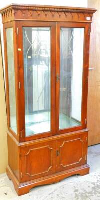 A mahogany finish display cabinet, with a moulded dentil cornice, raised above two glazed doors, above double panelled cupboards on bracket feet, 163cm high, 80cm wide, 37cm deep.