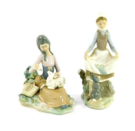 A Lladro porcelain figure of a girl standing before a rabbit, 23cm high, and a further group modelled as a seated girl feeding a lamb, 18cm wide. (2)