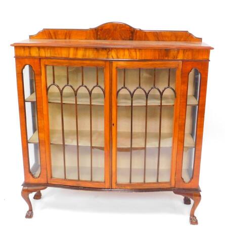 An early 20thC serpentine walnut display cabinet, with a pair of glazed doors opening to reveal two shaped shelves, glazed sides, raised on cabriole legs and ball and claw feet, 136cm high, 121cm wide, 37cm deep.