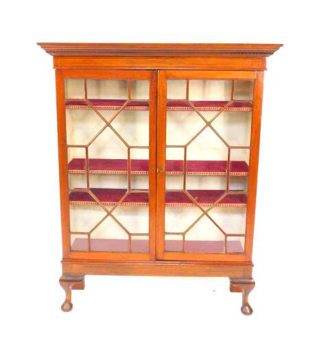 A Georgian and later mahogany display cabinet, the outswept pediment with dentil moulding, two glazed doors opening to reveal three velvet lined shelves, on a later base raised on cabriole legs, 139cm high, 110cm wide, 29.5cm deep.