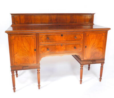 A George IV mahogany and ebony line inlaid sideboard, with splash back, two central drawers flanked by a pair of cupboard doors, raised on turned and fluted cylindrical legs, 112cm high, 151.5cm wide, 54cm deep.