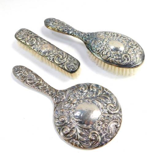 A silver backed three piece dressing table set, embossed with masks, birds and foliate scrolls, comprising hand mirror, clothes and hair brushes, Birmingham 1979.