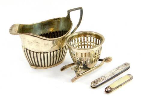 A silver semi fluted cream jug, hallmarks worn, 2.11oz., a silver plated egg cup on a wishbone stand, silver folding pocket knife case embossed with flowers and rococo scrolls, Birmingham 1899, and a further pocket knife. (4)