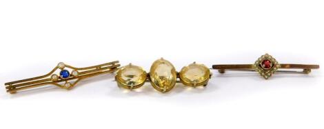 An Edwardian sapphire and seed pearl bar brooch, set in yellow metal, garnet and seed pearl bar brooch, and a further brooch set with three citrine coloured stones, in yellow metal. (3)