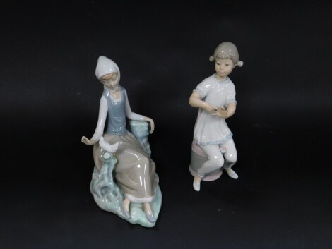 A Lladro porcelain figure modelled as a seated girl with a dove, and a further figure of a seated girl painting her fingernails, both boxed. (2)