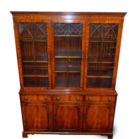 A Georgian style mahogany cupboard bookcase possibly Reprodux, the dentil moulded cornice over three glazed doors opening to reveal nine shelves, above three drawers over cupboards, on ogee bracket feet, 199cm high, 150cm wide, 36cm deep.