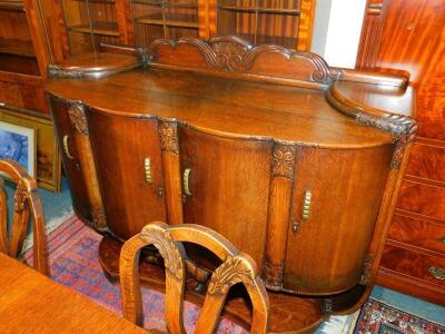 A Continental early 20thC oak dining room suite, stylistically carved with flowers and scrolling leaves, comprising a serpentine wardrobe, with carved splash back, having four doors enclosing drawers, shelves and a bottle stand, raised on a shaped base, 1 - 3