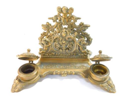 A Victorian style brass desk stand, cast with cherubs, fruit and flowers, with letter rack pen tray and pair of ink wells, 30cm wide.