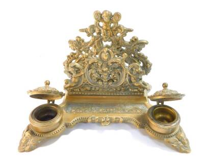 A Victorian style brass desk stand, cast with cherubs, fruit and flowers, with letter rack pen tray and pair of ink wells, 30cm wide.