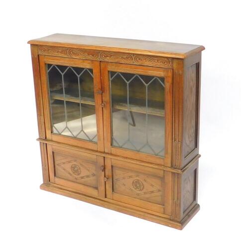 An Inglesants oak cupboard bookcase, with two glazed doors opening to reveal a single shelf, over a pair of carved cupboard doors, raised on a plinth base, 91cm high, 93cm wide, 24.5cm deep.