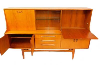 A G-Plan Fresco teak sideboard, with a pair of glazed central doors opening to reveal a lit single shelf unit, flanked by a drop down flap drinks cabinet, and sliding door opening to reveal a single shelf compartment over three drawers flanked by two pai - 2