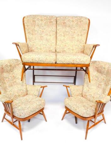 A vintage Ercol light oak three piece cottage suite, upholstered in floral fabric cushions, comprising two seater sofa, 141cm wide, and a pair of armchairs.