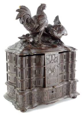 A late 19thC/early 20thC Black Forest carved jewellery box, the hinged lid decorated with chickens, leaves, etc., enclosing a fitted interior with six separate compartments, overall carved to simulate a house or country house on bun feet (AF), 38cm high,