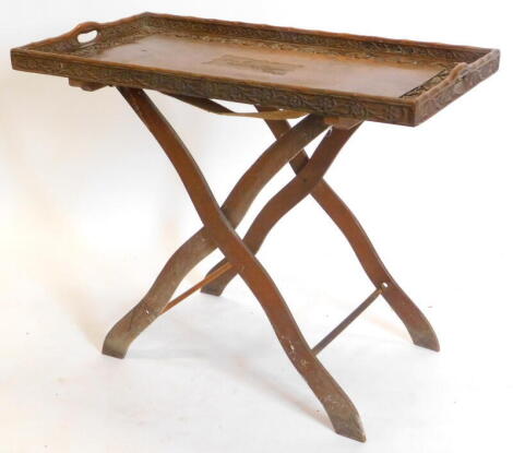 An Indian hardwood rectangular tray table, the galleried top carved with flowers, leaves, etc. and with an inscription "Anita October 29th 1913 Srinagar", on 'X' shaped support, 78cm wide.