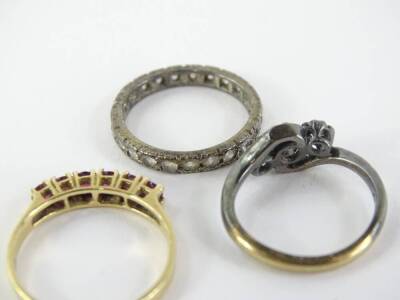 Three dress rings, comprising a ruby set half hoop eternity ring, yellow metal stamped 14K, with size round brilliant cut rubies, together with a 9ct gold and silver crossover dress ring and a further eternity ring, unmarked, the 14ct ring 3.4g all in (3) - 2