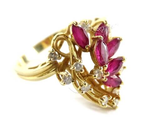 A modern dress ring, with floral type spray centre, set with oval cut rubies and round brilliant cut diamonds, in swirl setting, on a two row band, yellow metal stamped 14K, ring size M½, 4.3g all in.