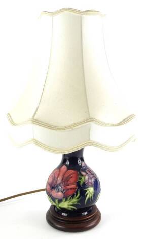 A Moorcroft pottery baluster shaped lamp base, decorated with poppies, on a navy blue ground, with composition base and cream shade, 43cm high.