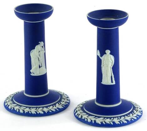 A pair of dark blue Wedgwood Jasperware candlesticks, each decorated with neo-classical figures and a band of oak leaves, 15cm high.